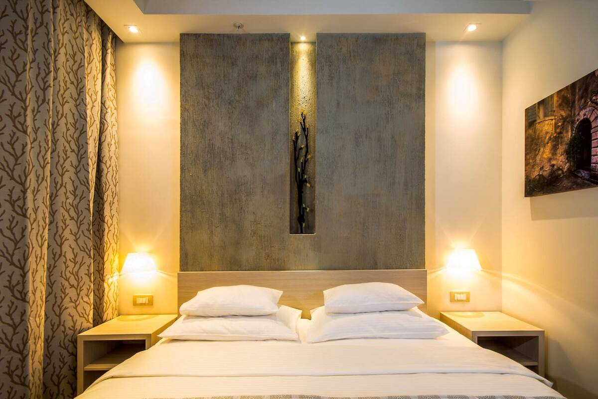 A hotel room with a large bed, two bedside tables, a wall-mounted artwork, and a patterned curtain.