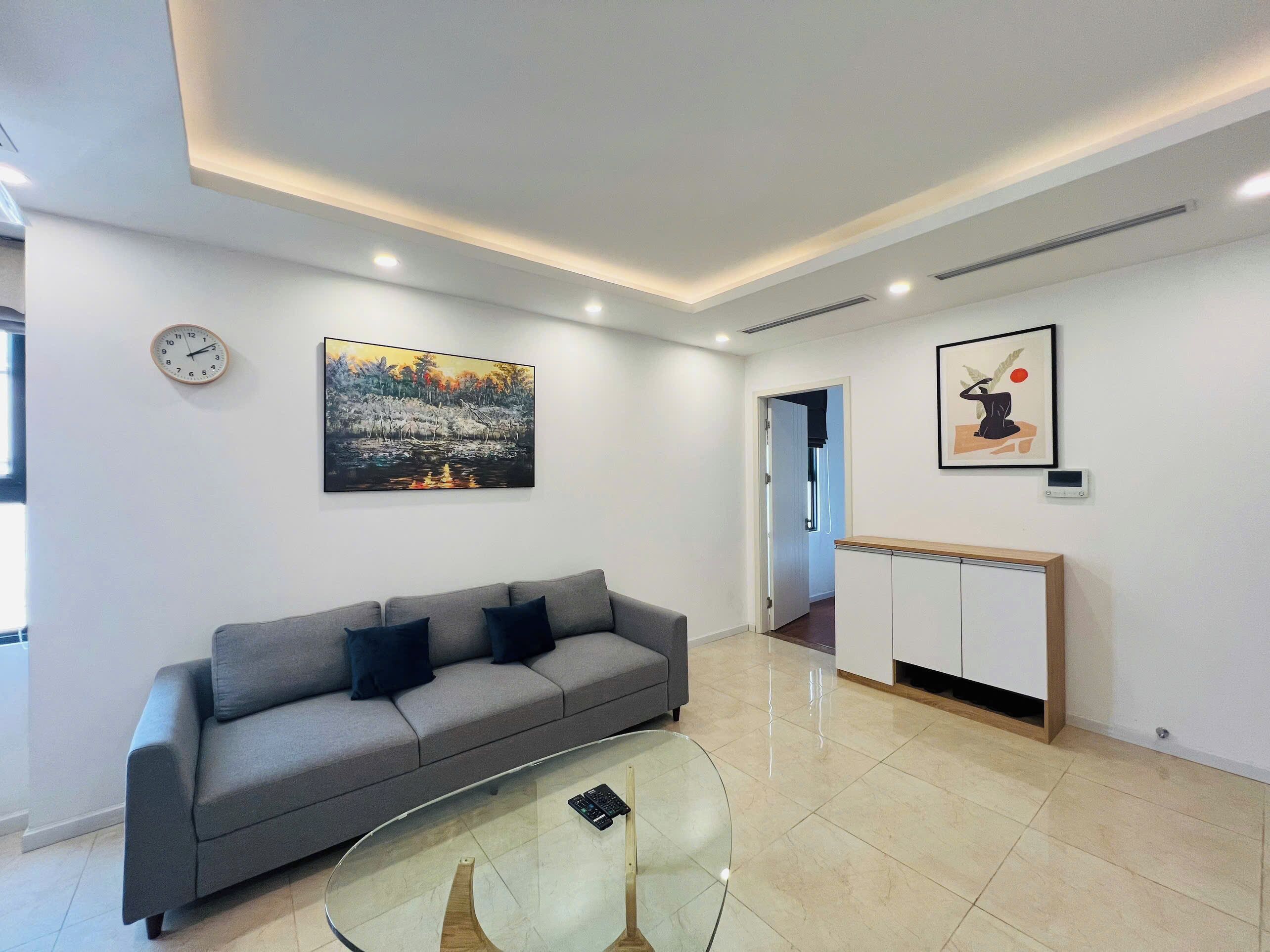 Ein modernes Wohnzimmer mit einem grauen Sofa, einem Glastisch und Kunstwerken an den Wänden.