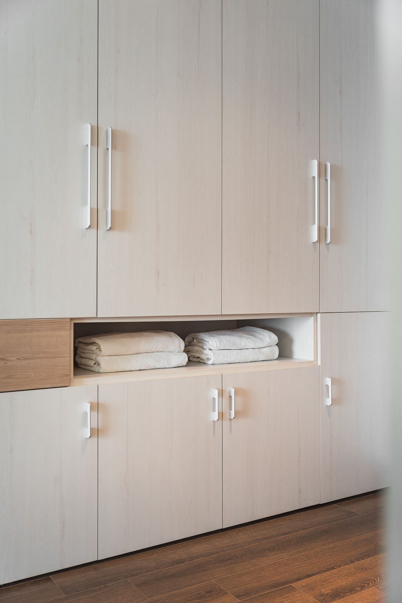A wooden wardrobe with white handles, a shelf with folded towels, and a wooden floor.