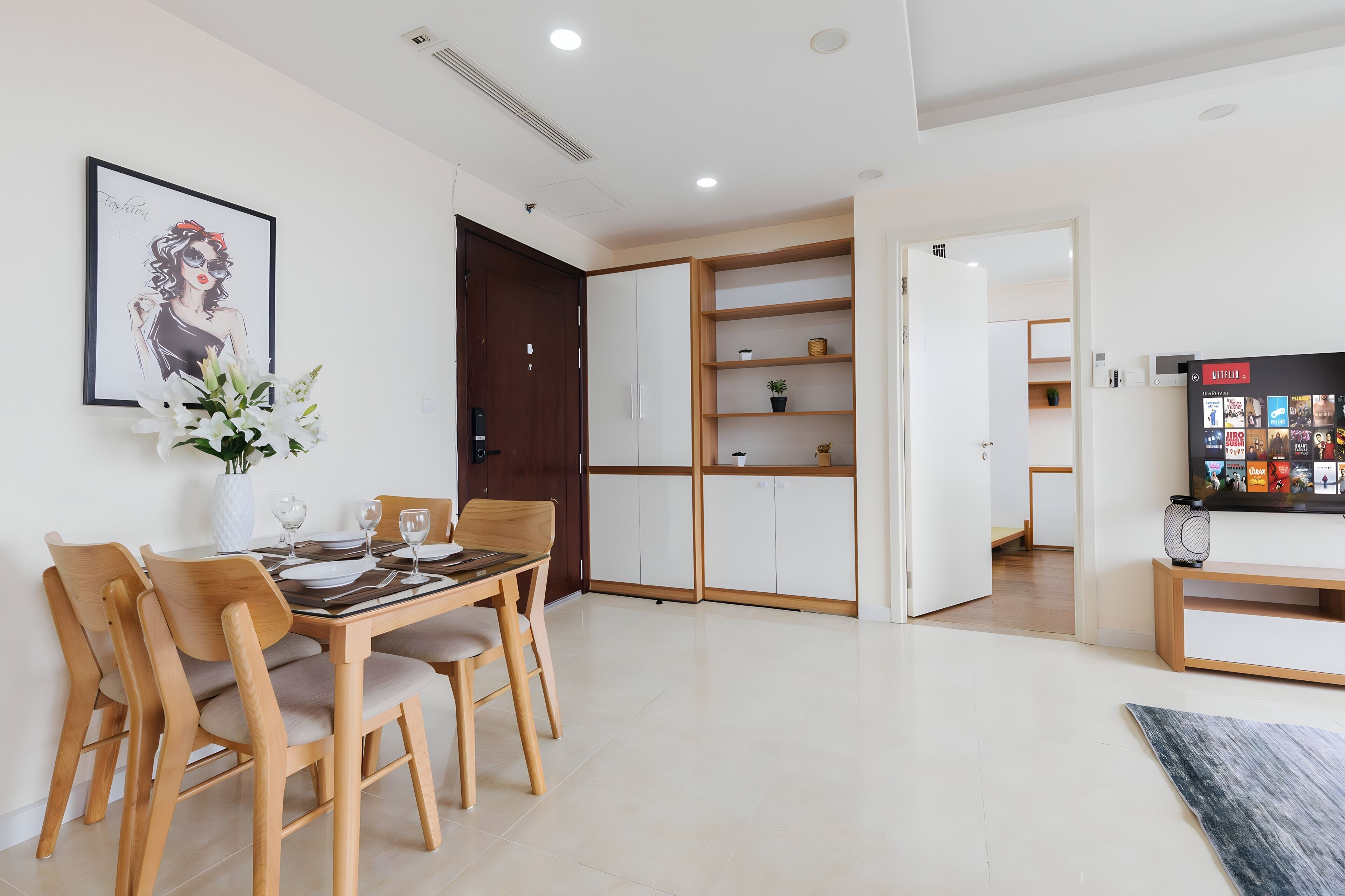 A modern dining area with a wooden table and chairs, a vase of flowers, and a framed artwork on the wall.
