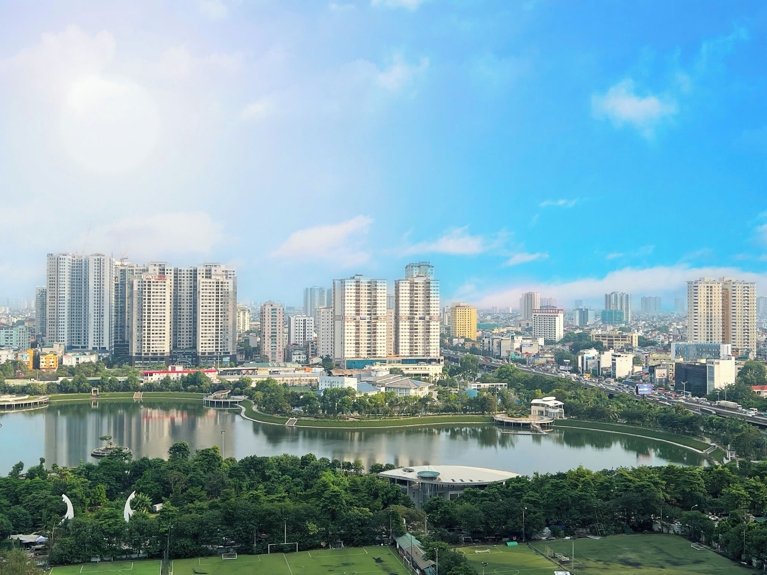 Un paysage urbain avec de hauts immeubles, un lac et un parc doté d’un terrain de football.