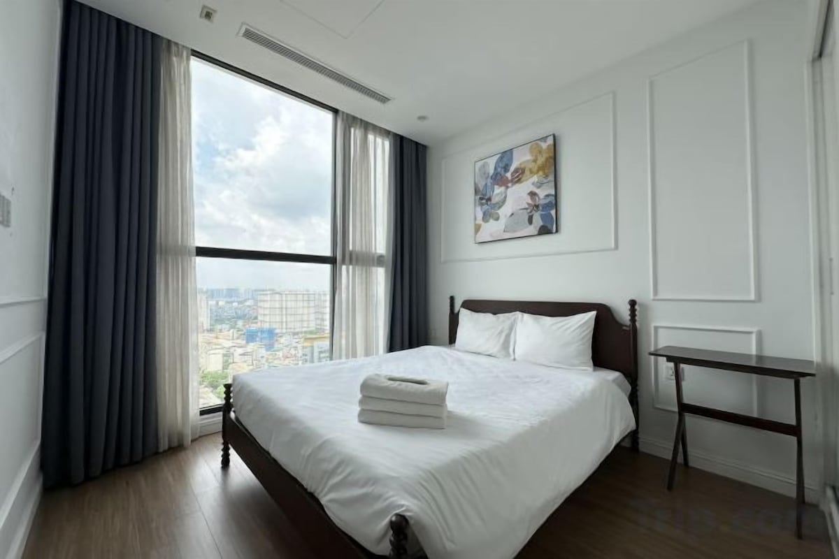 Een hotelkamer met een groot bed, een nachtkastje, een raam met gordijnen en uitzicht op de stad.