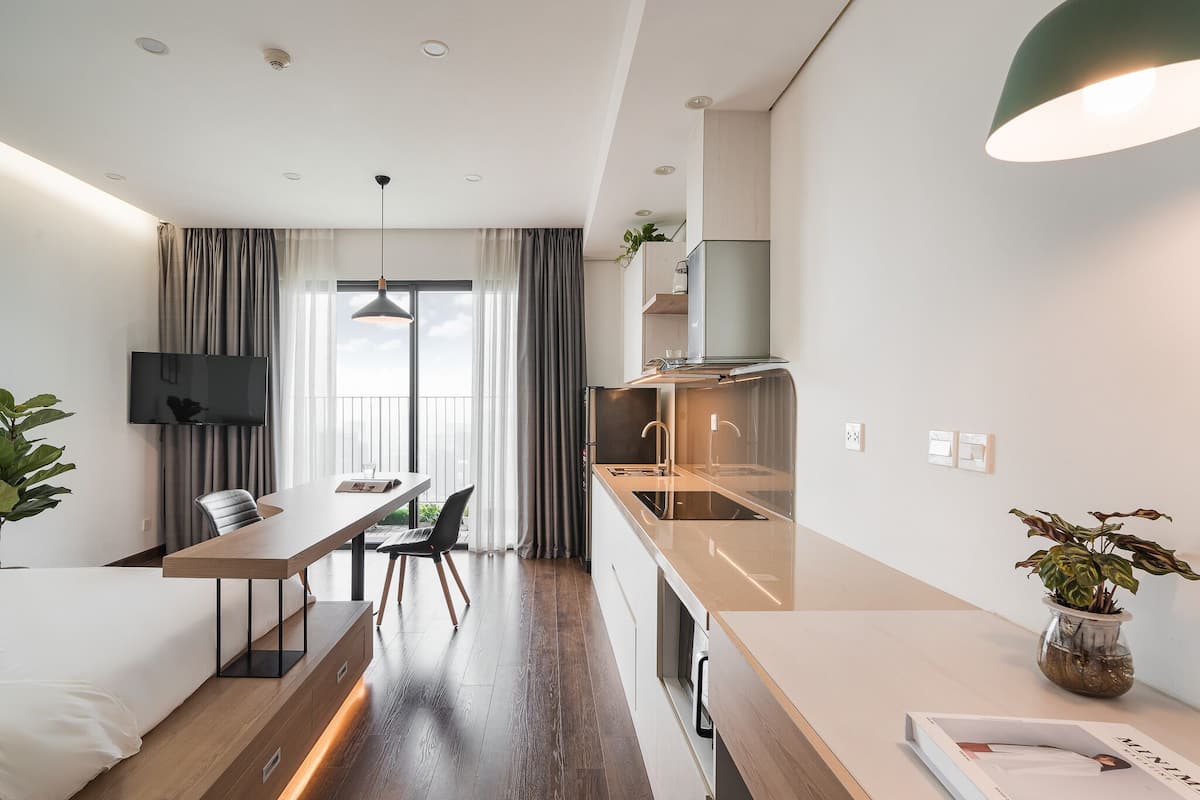 Een moderne hotelkamer met een kitchenette, een eethoek en een groot raam met gordijnen.