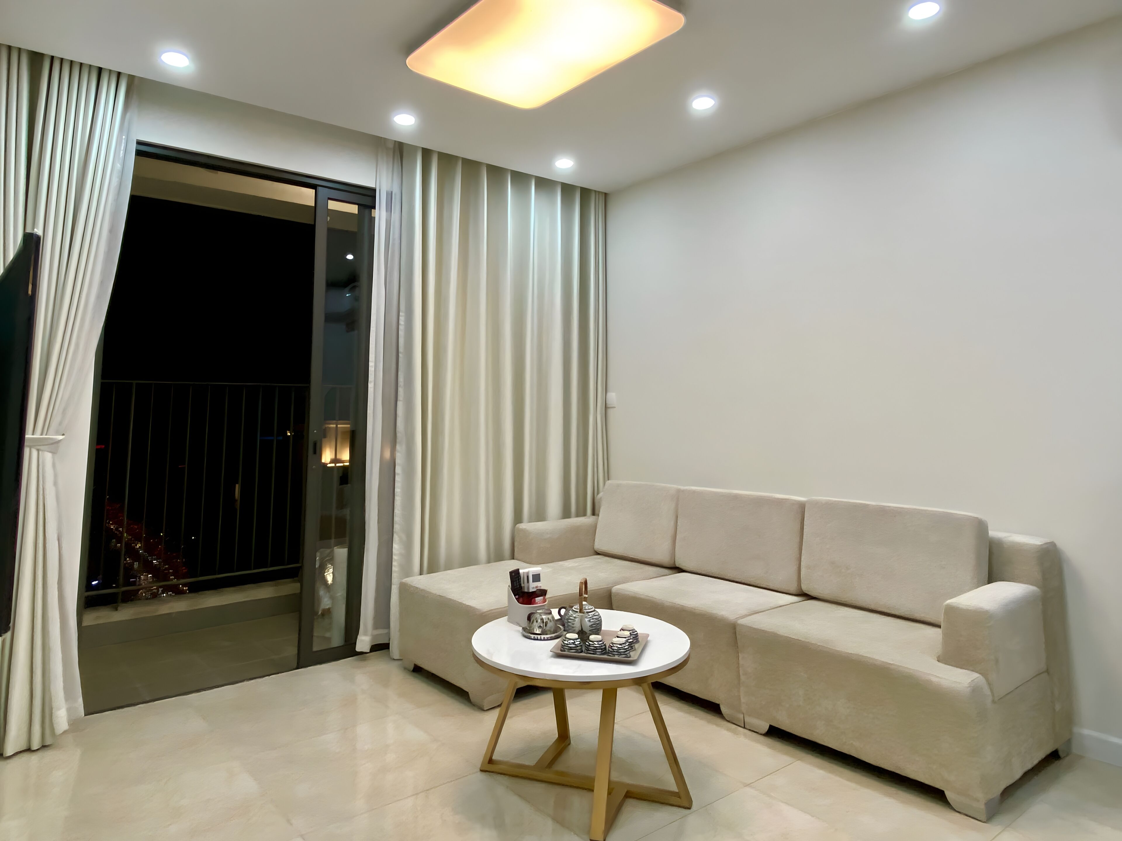 Ein modernes Wohnzimmer mit einem beigefarbenen Sofa, einem runden Couchtisch und einer Glasschiebetür, die auf einen Balkon führt.
