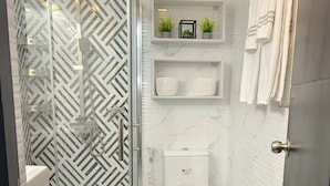 Un baño con cabina de ducha de vidrio, inodoro blanco, azulejos de mármol y un perchero para toallas.