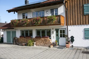 A two-story building with a balcony, a wooden fence, and a variety of potted plants. - Vacation apartment with a separate bedroom, balcony, near downtown, quiet, 44 m² (Prien am Chiemsee)