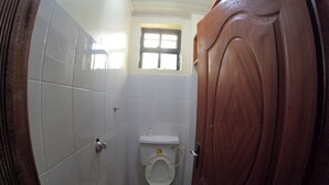 Een kleine, praktische badkamer met witte tegels, een houten deur en een raam boven het toilet.