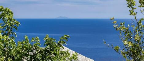 A coastal view with a stone building, lush greenery, and a clear blue sea.
