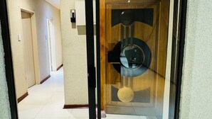 A hallway with a glass door leading to a room with a wooden door and a circular object on the floor. - Icebolethu Guest House (Lekwa)