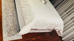 A neatly made bed with white linens and a fluffy pillow, a bedside table with a lamp, and a patterned rug on a wooden floor. - Icebolethu Guest House (Lekwa)
