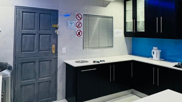 A modern kitchen with black cabinets, a white countertop, and blue LED lighting on the ceiling. - Icebolethu Guest House (Lekwa)