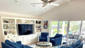A modern living room with a blue sofa, a glass coffee table, and a TV on a white entertainment unit.