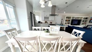 A dining area with a white table and chairs, a kitchen in the background, and a blue sofa.