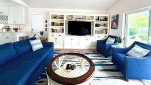 A modern living room with blue sofas, a coffee table, and a TV on a white entertainment unit.