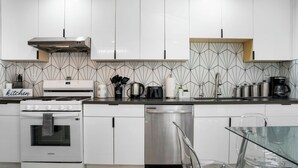 Una cocina moderna con armarios blancos, un lavavajillas de acero inoxidable, un horno Samsung y una cafetera.