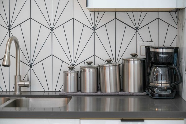 Una cocina con un salpicadero geométrico moderno, contenedores de acero inoxidable y una cafetera.