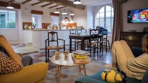 A cozy living room with a kitchen in the background, wooden beams, and a television on the wall. - Cottage in Clisson by the Sèvre River (Clisson)