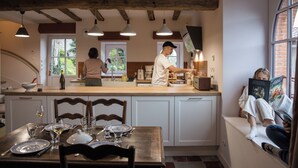 A kitchen with a dining area, wooden beams, pendant lights, and a person reading a book. - Cottage in Clisson by the Sèvre River (Clisson)
