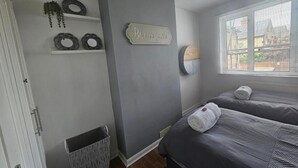 Un dormitorio con dos camas, una ventana con persianas, un letrero en la pared y un pequeño cubo de basura.