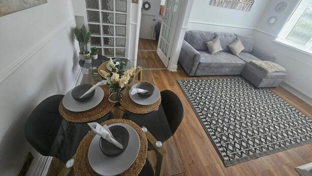Un comedor con una mesa dispuesta para cuatro, un sofá gris y una alfombra estampada.
