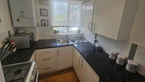 Una cocina con armarios blancos, encimera negra, estufa y ventana con persianas.