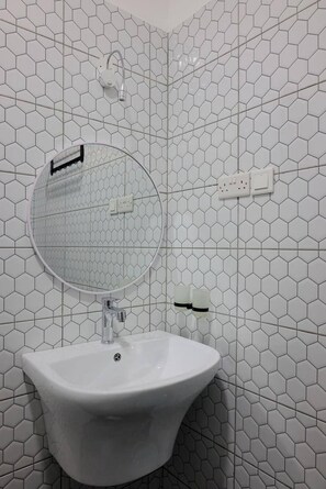 A bathroom with a white sink, a round mirror, and a hexagonal tile pattern on the walls. - The Residence Ug (Kampala)