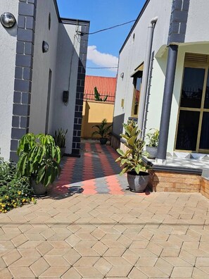 A narrow alleyway with potted plants and a tiled walkway leading to a building with a yellow facade. - The Residence Ug (Kampala)