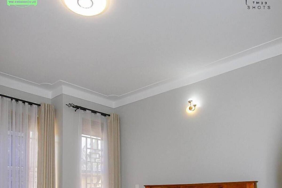 Una camera da letto con un letto in legno, tende bianche, un comodino e una lampada a parete.