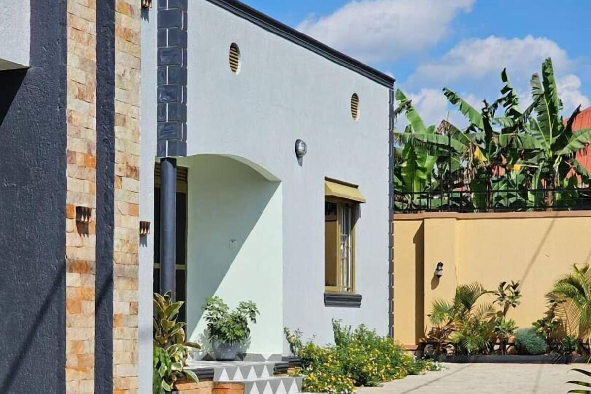 Un edificio moderno con una facciata pulita e geometrica, un cortile lastricato e vegetazione circostante.