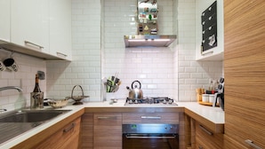 Eine moderne Küche mit weißen Fliesenspiegeln, Holzschränken, einer Edelstahlspüle und einem eingebauten Backofen.