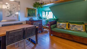Ein modernes Wohnzimmer mit Holzesstisch, grünem Sofa und Küchenbereich mit Fenster.