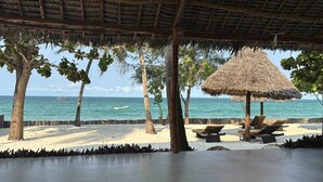 A beachside lounge with a thatched roof, palm trees, and a view of the sea. - MANOLO Beach Resort (Uroa)