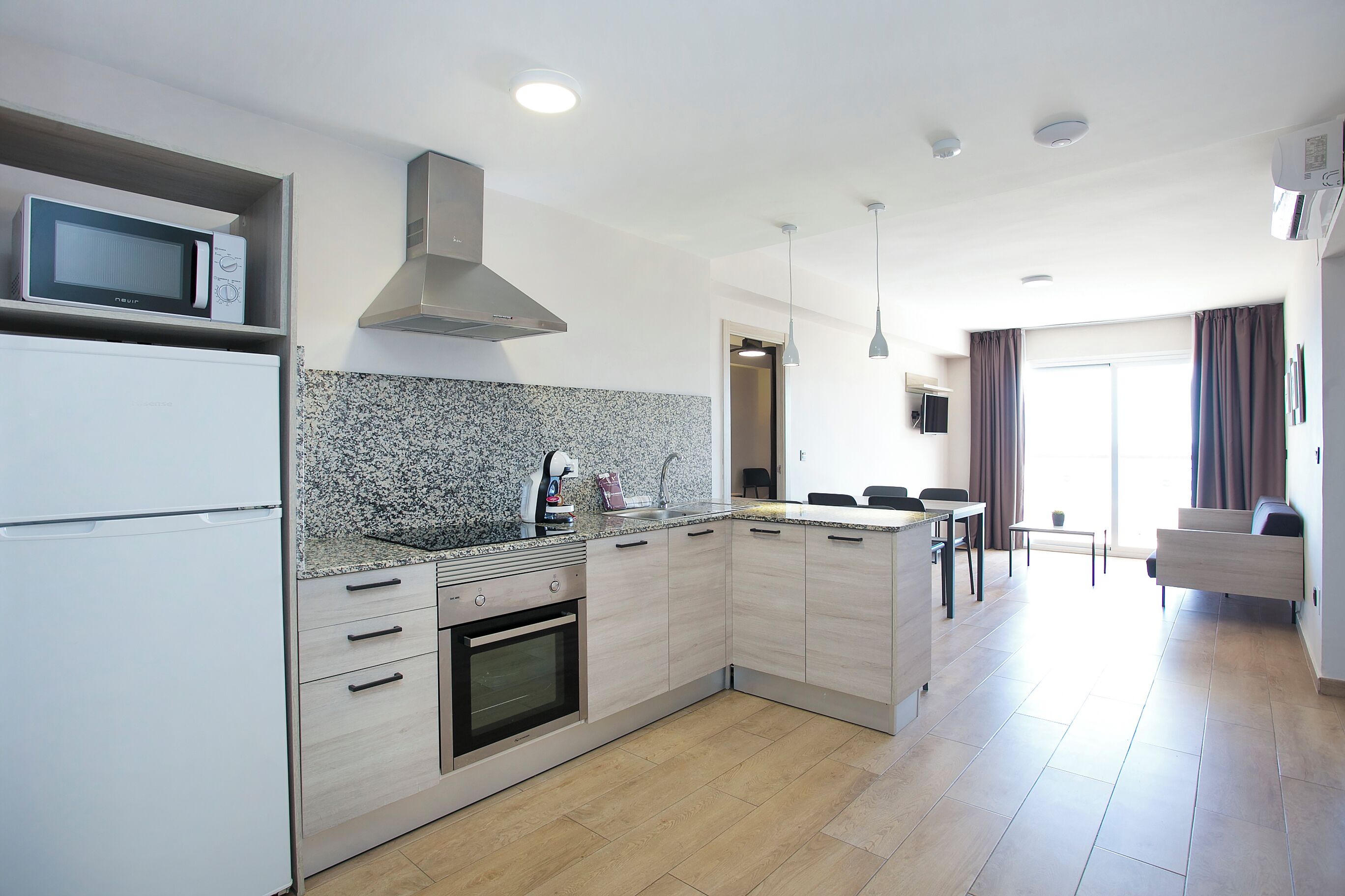 A modern kitchen with a microwave, oven, and granite countertop. There is a dining area with a table and chairs, and a living area with a sofa.