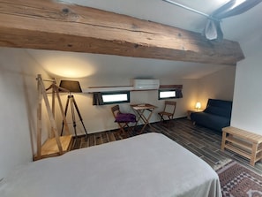 Cozy retreat with a bed, desk, and sofa, featuring exposed wooden beams and a tiled floor.
