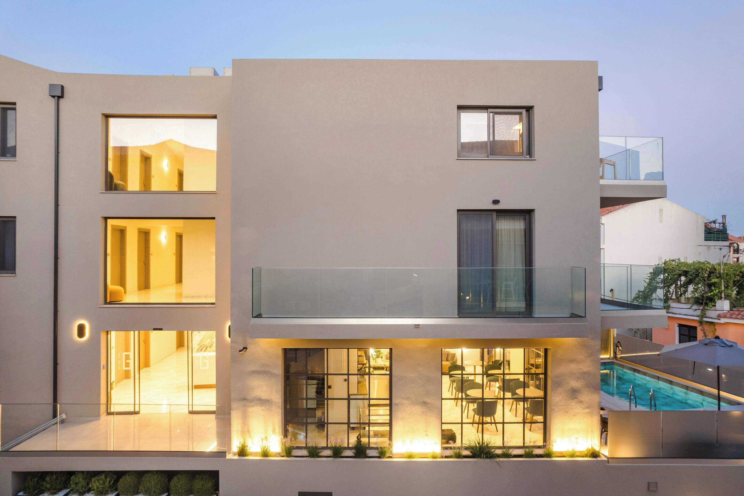 A modern multi-story building with large windows, a balcony, and a pool area.
