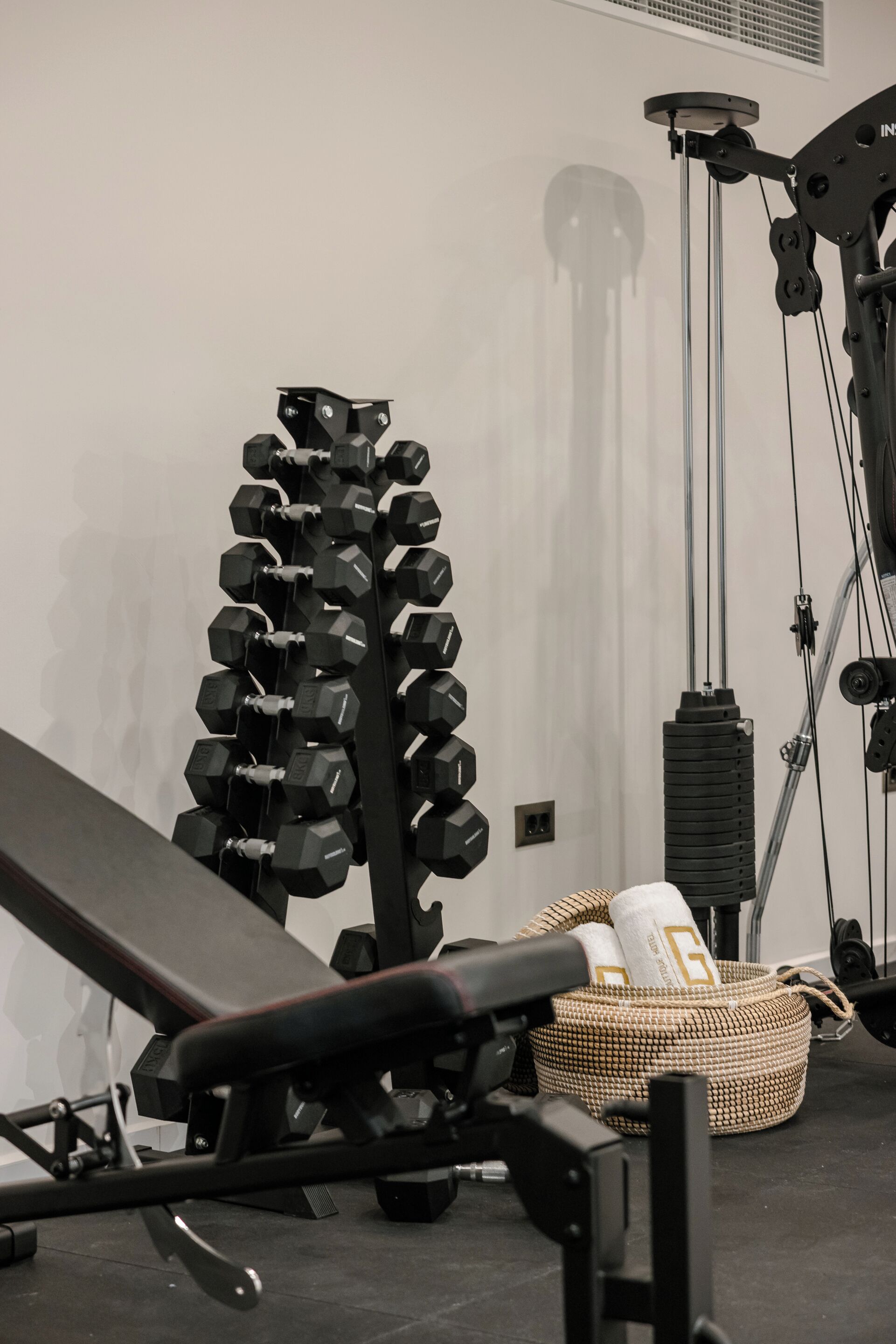 A gym with a bench, dumbbells, a basket, and weightlifting equipment.