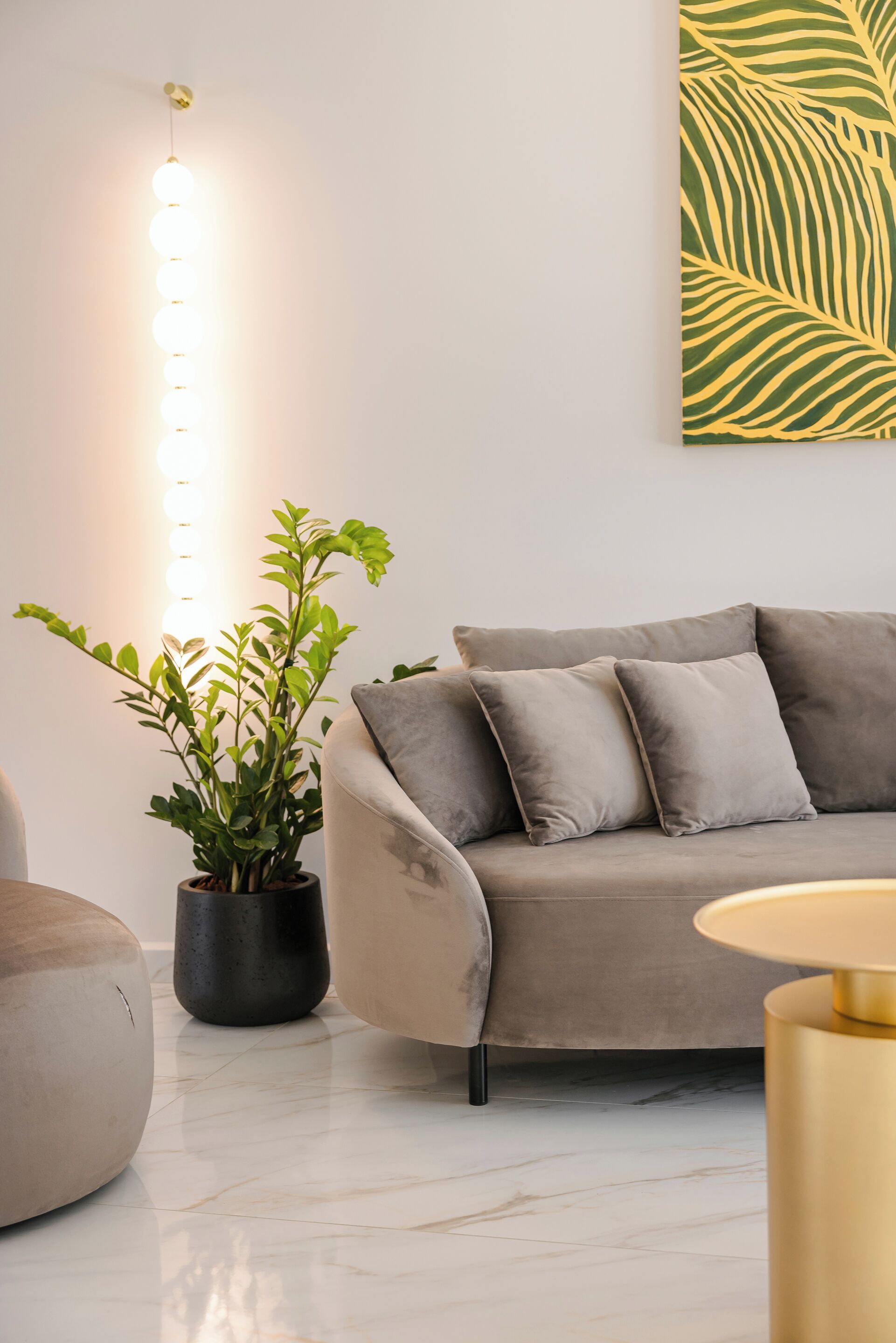 Un salon moderne avec un canapé gris, une plante en pot et un luminaire fixé au mur.
