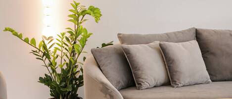 Un salon moderne avec un canapé gris, une plante en pot et un luminaire fixé au mur.