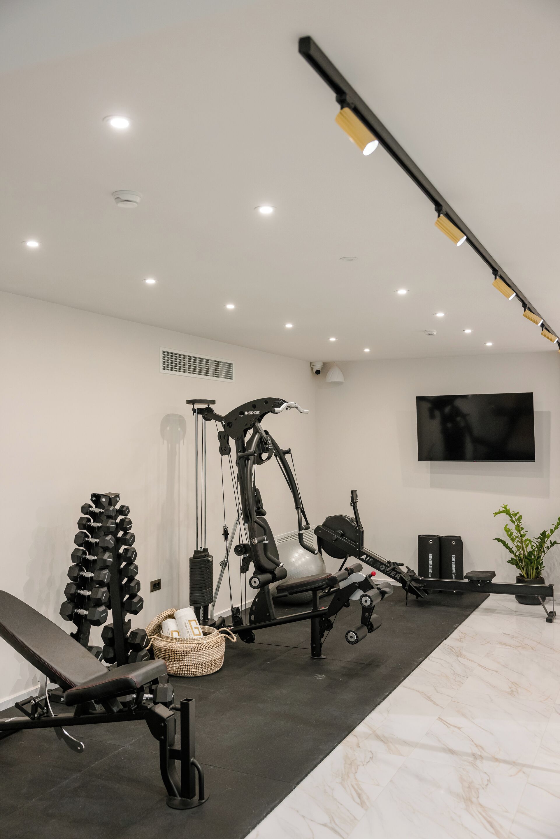 A modern gym with various exercise equipment, a wall-mounted TV, and a ceiling-mounted light fixture.