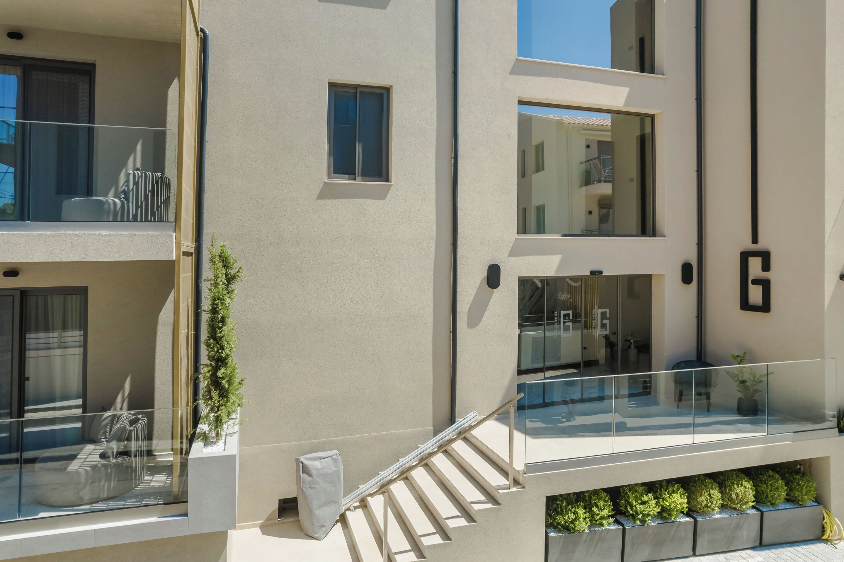 A modern building with a glass balcony, a staircase, and a small garden area.