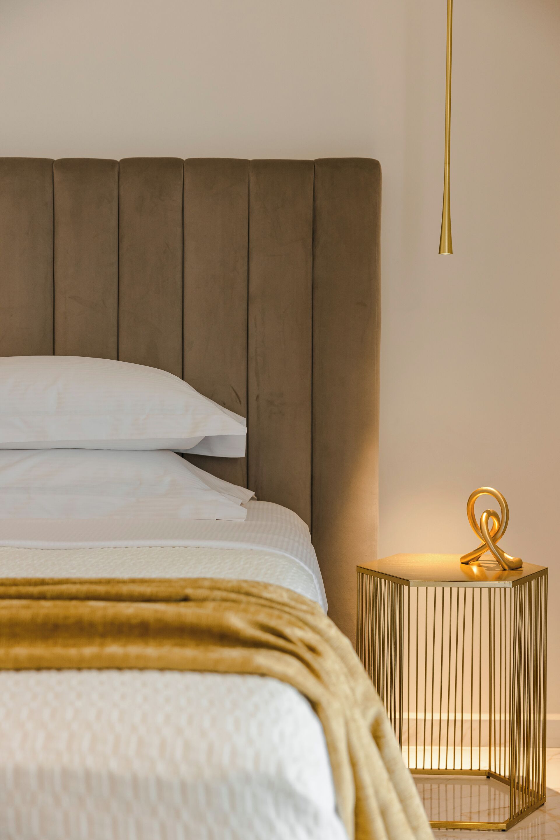 A bed with a headboard, white bedding, and a gold-colored throw blanket.