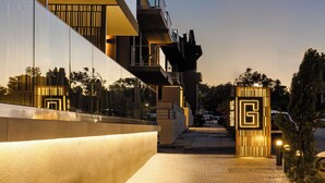 Una entrada de hotel moderna con fachada reflectante, un camino de ladrillo y un llamativo letrero con la letra 'G'.