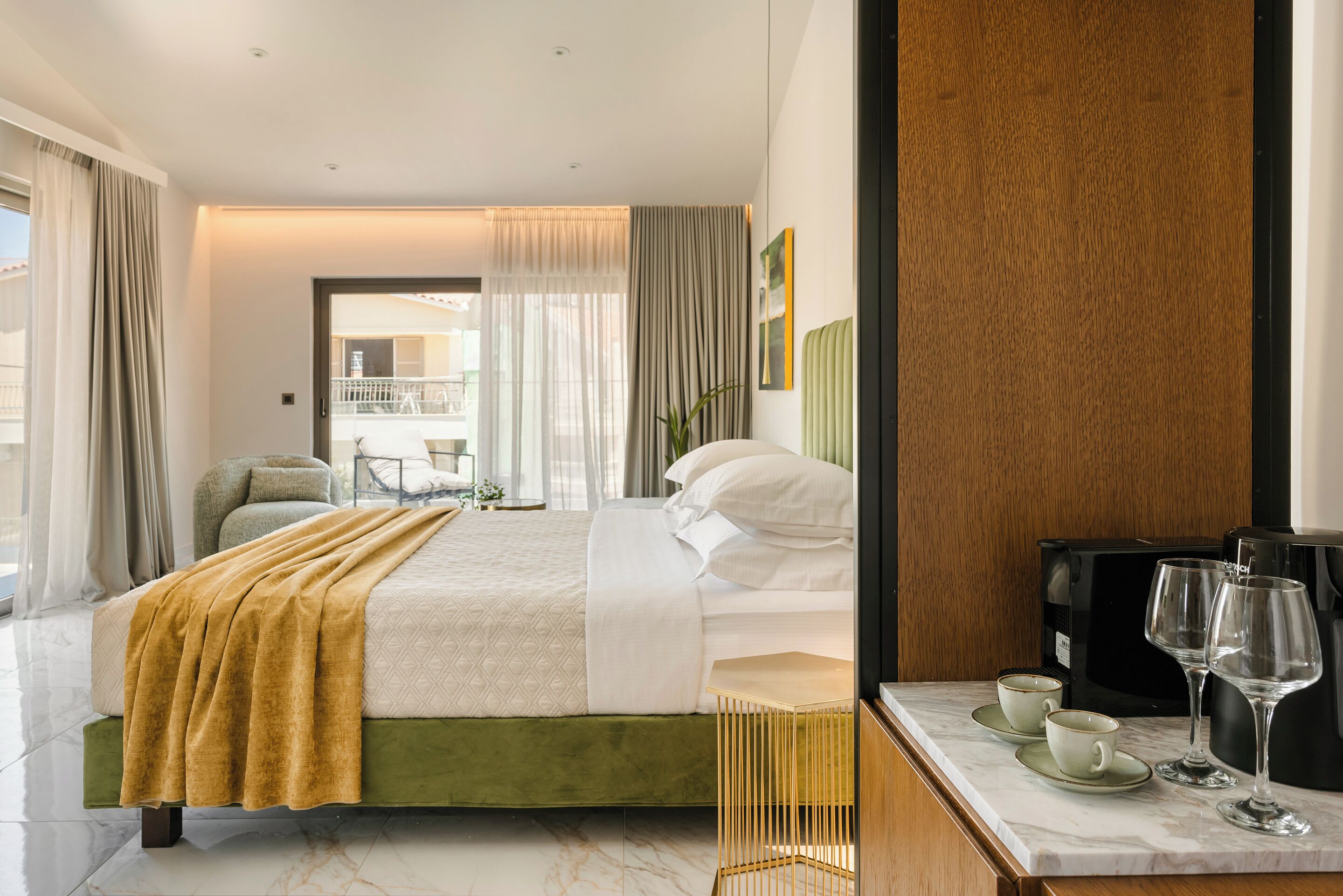 A hotel room with a bed, a coffee machine, and a table with cups and glasses.