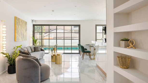 Una sala de estar moderna con un sofá, otomanas, un comedor y vistas al exterior.