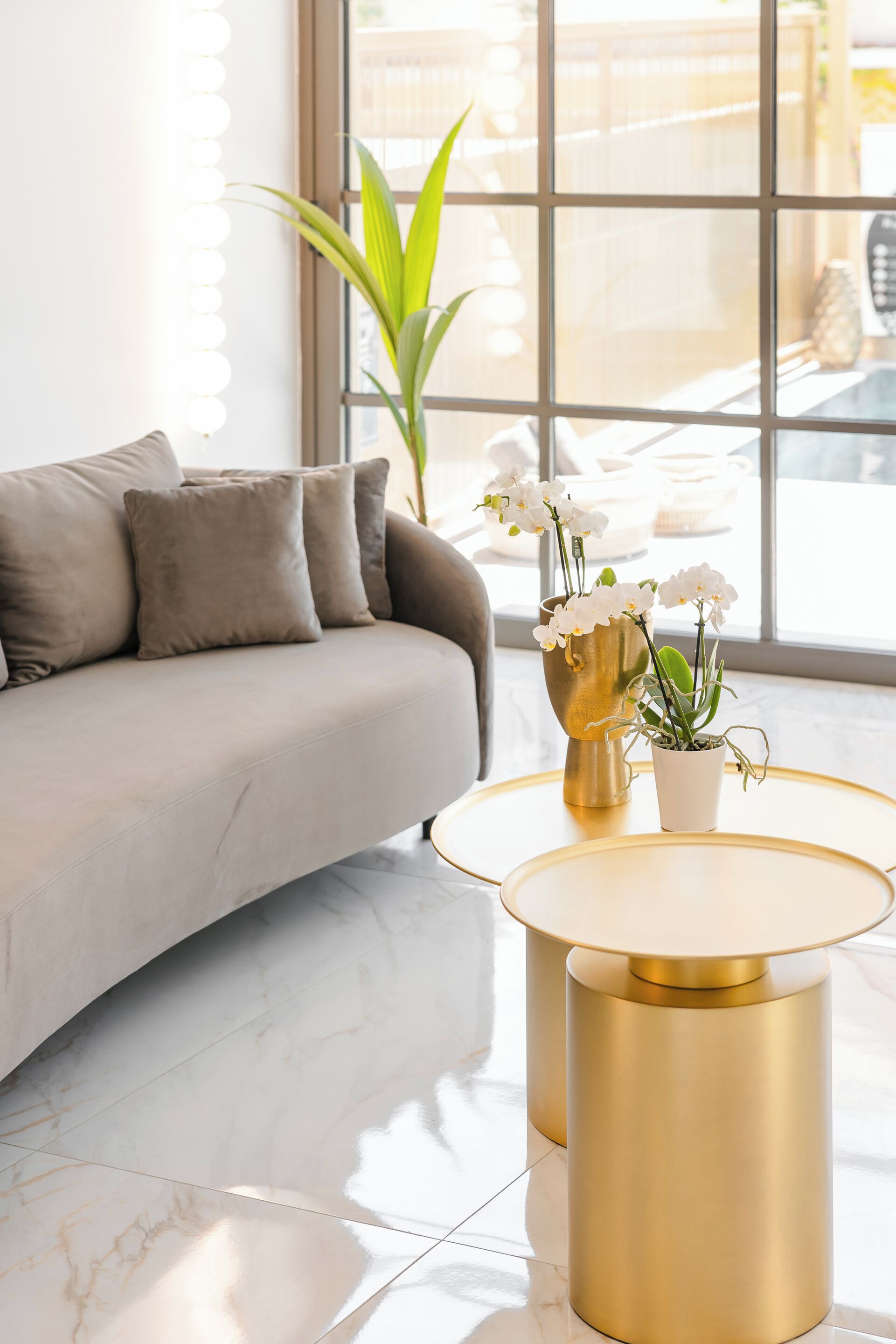 A modern living room with a sofa, a round gold table, and a potted plant.