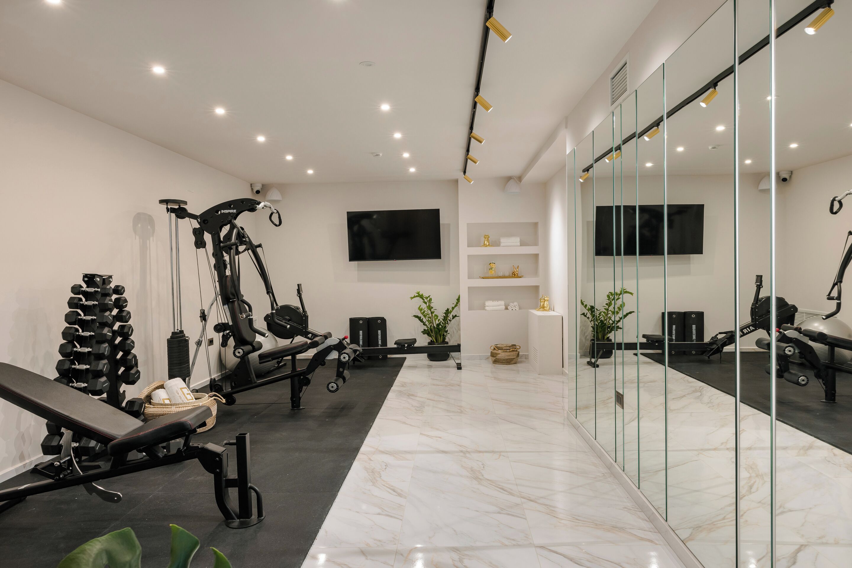A modern gym with exercise equipment, a large mirror, and a TV on the wall.