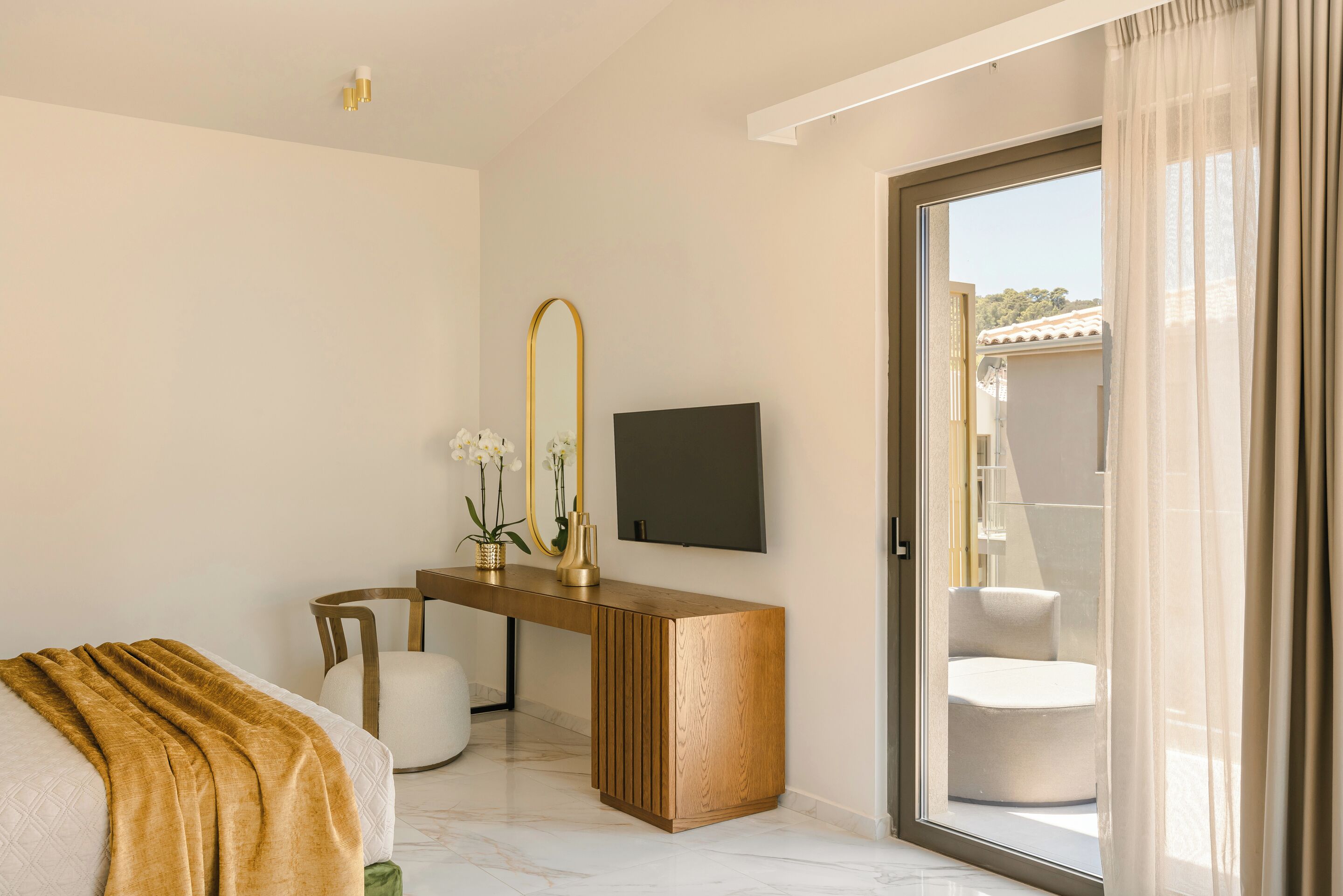 A modern bedroom with a bed, a wooden desk, a TV, and a sliding glass door to a balcony.