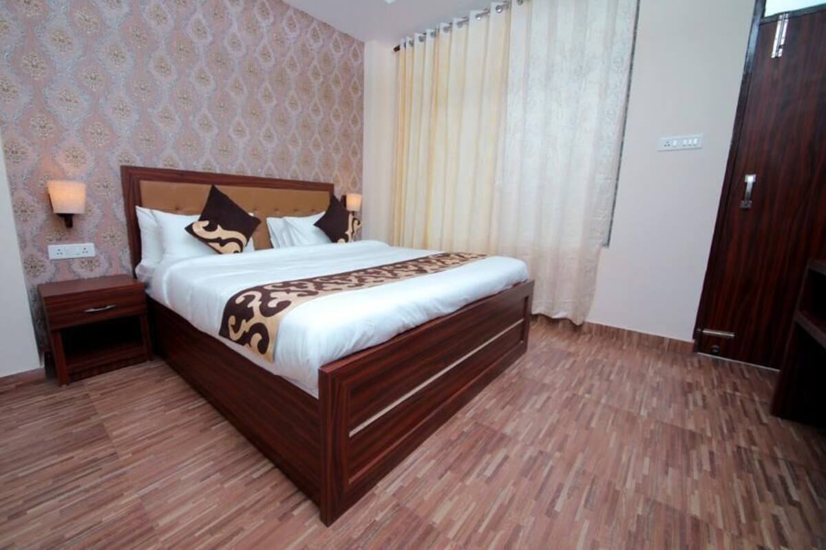 A neatly made bed with a wooden frame and a patterned bedspread, a nightstand with a lamp, and a patterned wallpaper on the wall.
