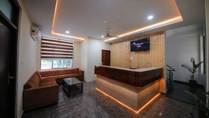 A reception area with a wooden reception desk, a sofa, and a television mounted on the wall. - Amritara Social Palace (Chinyalisaur)