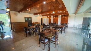 A spacious dining area with wooden tables and chairs, a high ceiling with hanging lights, and a glass partition wall. - Amritara Social Palace (Chinyalisaur)